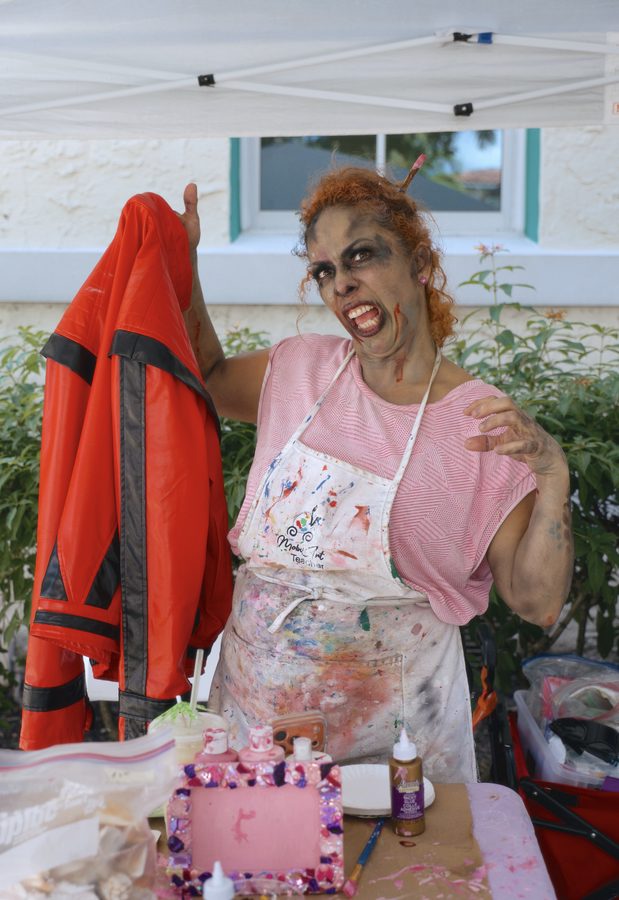 An art teacher in zombie make-up holding up a red Thriller jacket at her craft table.