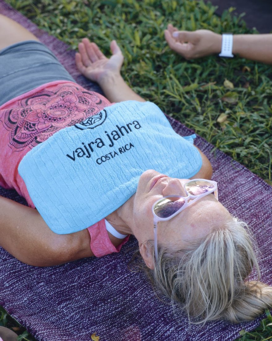 A guest resting in savasana on the grass with a Vajra Jahra cold towel across her chest.